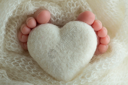 两只可爱的小小婴儿脚 裹在白毛毯上 还有由羊毛线织成的编织心脏图片