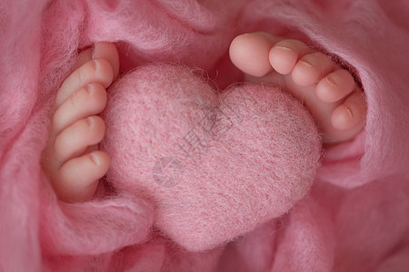 两只可爱的小婴儿脚 裹在粉红色的毛毯上 还有由羊毛线织成的编织心脏图片