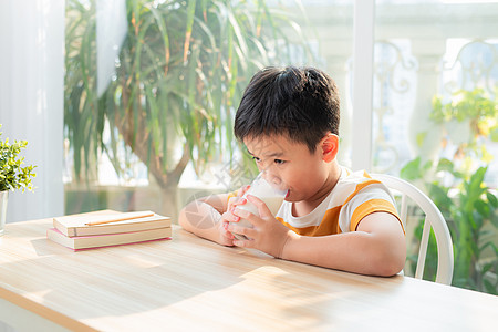 可爱男孩在做功课后坐在桌子上喝着牛奶的杯子活力奶制品饮食早餐童年乳糖玻璃孩子饮料食物图片