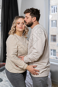 幸福家庭概念 丈夫拥抱肚子怀孕的孕妇 站在沙发附近的室内起居室房间微笑成人父亲男性母亲孩子女士妻子新生活图片