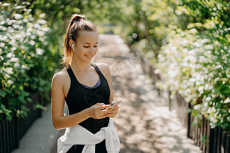 运动作为生活方式 专注于智能手机的健康苗条运动女性的水平镜头检查信息 并从穿着运动服的播放列表中选择歌曲 在户外呼吸新鲜空气图片