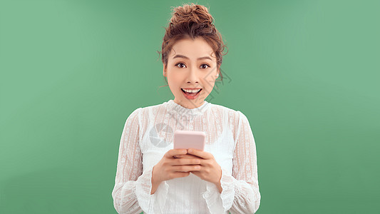 穿着白色T恤的年轻现代女性使用手机 女孩发短信和微笑 站在绿色背景上站立电话快乐细胞成人女士图片