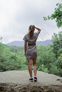 穿着暑期服装的年轻女青年 站在森林中的一块大石头上 向远看树干旅行树木自由森林植物木头林地场景荒野图片