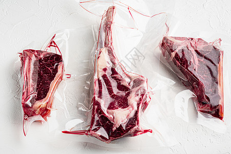 塑料袋中的肉类产品 托马霍克 t骨和俱乐部牛排切割 以白石为背景图片