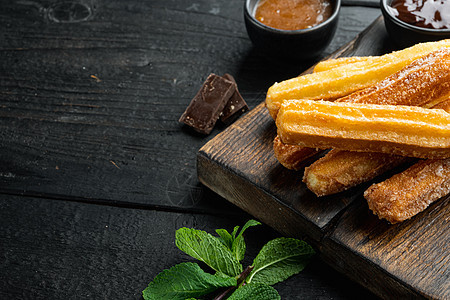 典型的西班牙零食churros 油炸面糕饼 通常配有巧克力焦糖辣酱 黑色木制餐桌背景和文字空间 复制空间图片