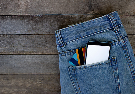 在木质背景上用空屏幕和口袋牛仔裤的信用卡装填智能手机 顶端视图 文本位置触摸屏互联网销售小样空白购物技术广告折扣工具图片