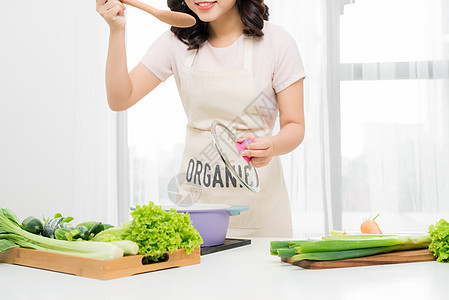 美丽的年轻女子在家里用蔬菜煮汤的肖像 笑声女性饮食家庭女士主妇厨房蓝色食物围裙食谱图片