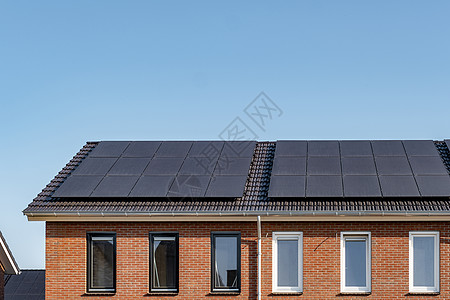 在阳光明媚的天空下 屋顶上附有太阳能电池板的新建房屋特写带有黑色太阳能电池板的新建筑 翻译 太阳能电池板 太阳能技术生态细胞控制图片