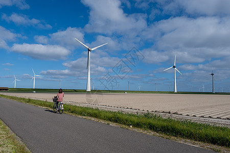 风车农场旁的年轻女性电动绿色自行车 风车在美丽明亮的日子里与世隔绝 荷兰涡轮能源公园天空技术场地生态植物发电机海洋图片