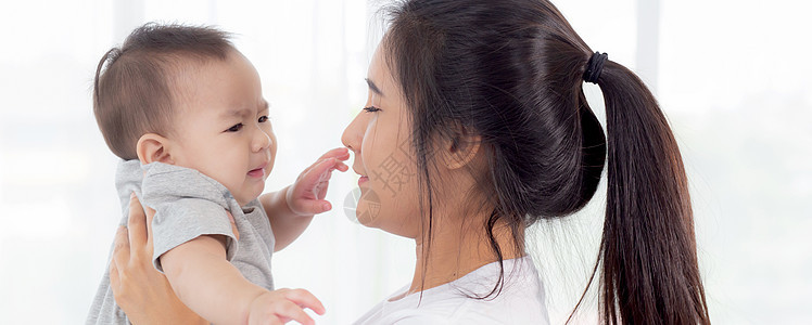 年轻的亚洲母亲在家里的卧室里抱着小女婴 妈妈带着孩子和照顾孩子 女人和孩子无忧无虑 蹒跚学步的孩子和父母 情感和表达 家庭观念女图片