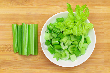 白色碗里带水滴的新鲜切菜小棍子桌子减肥植物木板食物芹菜梗芹菜生食盘子树叶图片