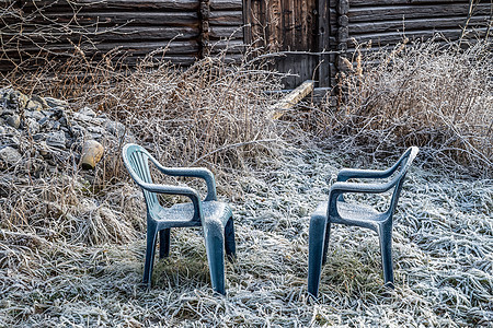 乡村花园里的两张蓝色塑料椅 上面有冰冻的霜 乡村的农舍和草地覆盖着冰冷的白霜 在乡村的一个初冬早晨-从秋季到冬季突然冻结温度的概图片