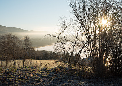 日出时 田园诗般的农田 湖泊和山脉上雾气缭绕的农业自然景观 初秋的清晨 阳光穿过树木 地面上有白霜图片