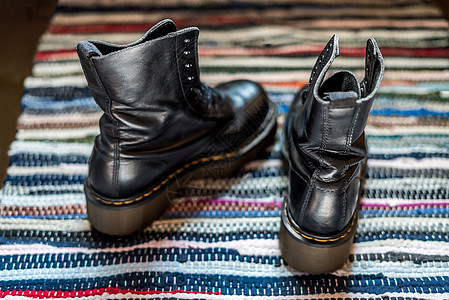 背对着两双黑色黑脚踝皮靴的景象 穿在色彩多彩的地毯上 作为泡水者的概念图片
