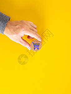 在黄色背景上放置蓝色购物车图标的男性手图片