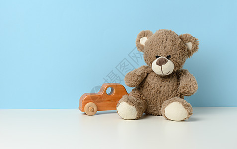 棕褐色可爱泰迪熊坐在白桌和木童玩具车上 蓝底图片