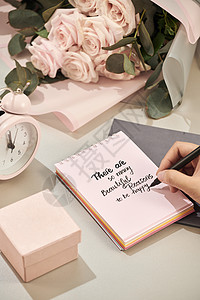 女人手里拿着笔 准备写 粉红玫瑰 笔和礼物 白色桌子上有粉红色的心 爱情观 圣瓦伦丁节的概念 母亲节的概念纪念日周年问候语婚礼红背景图片