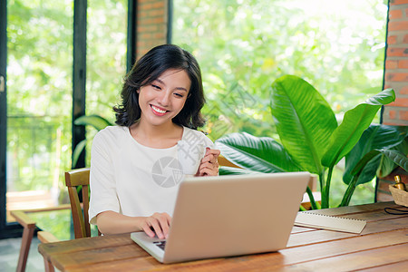 美丽的年轻微笑的女士 在大窗户附近的笔记本电脑上工作图片