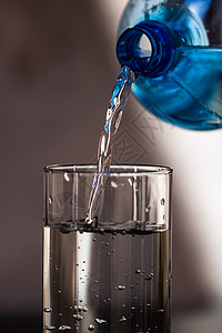 将蓝塑料瓶的水从蓝色塑料瓶浸入底底模糊的玻璃杯中 选择焦点 浅度DF和复制空间运动水瓶矿物液体瓶子气泡流动玻璃水滴口渴图片