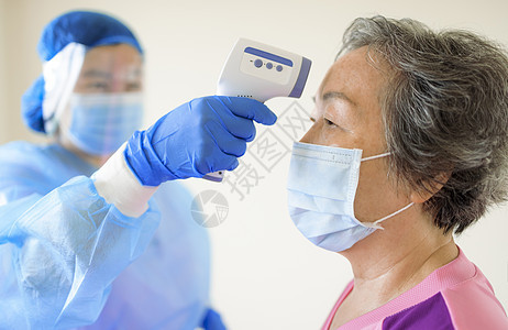 护士使用红外温度计设备检查高龄妇女前额的温度;在高级女性的前额进行化验图片