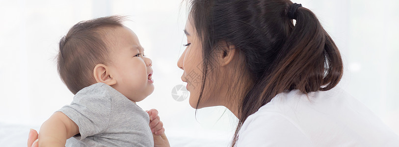 年轻的亚洲母亲在家里的卧室里抱着小女婴 妈妈带着孩子和照顾孩子 女人和孩子无忧无虑 蹒跚学步的孩子和父母 情感和表达 家庭观念新图片