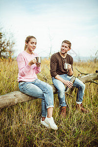 欢快的情侣喝热咖啡或茶叶 坐在户外木木木木桩上交流沟通信息服装咖啡杯友谊活动幸福休闲两个人团结田园微笑图片