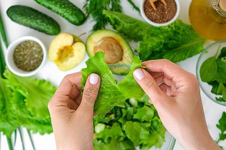 烹调新鲜的绿色蔬菜和草本沙拉的妇女 生食概念 素食菜单 烹饪健康饮食或素食 女手切沙拉 周围环绕着绿色蔬菜 一步一步的食谱食物营图片