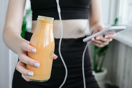 千禧一代的年轻女性正在检查智能手机喝纯素冰沙饮料排毒 在家做瑜伽练习的女人 在线学费清洁饮食 减肥 健康节食食品概念 保持健康微图片