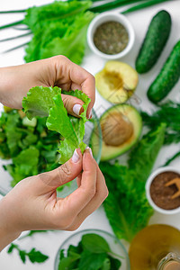 烹调新鲜的绿色蔬菜和草本沙拉的妇女 生食概念 素食菜单 烹饪健康饮食或素食 女手切沙拉 周围环绕着绿色蔬菜 一步一步的食谱黄瓜女图片