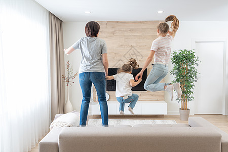 母亲和两个女儿在客厅沙发上跳起沙发玩得开心家庭生活享受童年微笑乐趣父母长椅妈妈摄影闲暇图片