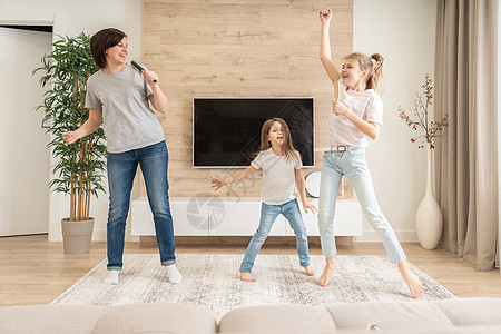 快乐的母亲和两个女儿在梳子里唱卡拉 OK 歌曲很开心 妈妈笑着在家里和十几岁的女孩一起享受有趣的生活方式活动舞蹈麦克风喜悦乐趣卡图片