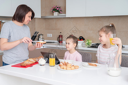 母亲和两个女儿一起吃早餐 幸福的单身母亲家庭概念与家人一起共进早餐健康饮食成人药片女孩桌子父母微笑果汁女士面包背景