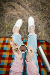 在大自然中野餐或吃零食 女性双手捧着一杯茶和一个三明治 坐在草地上吃零食的年轻女人或少女 特写镜头 高角度视图图片