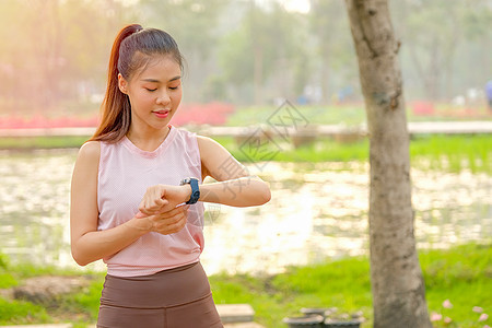 年轻美丽的运动女孩的肖像看着她的手表 带着晨光呆在公园或花园里赛跑者监视器跑步身体运动员训练女性技术休息成人图片