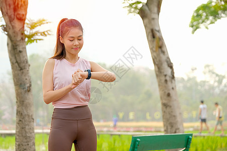 年轻美丽的运动女孩的肖像看着她的手表 带着晨光呆在公园或花园里赛跑者运动员慢跑者技术女性休息身体训练跑步成人图片