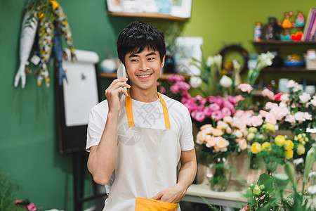 在花店用手机聊天时 年轻英俊的花匠写字单顾客商业命令潮人销售电话男人男性植物零售图片