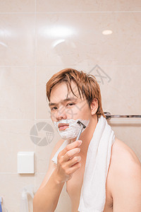 英俊的年轻人在浴室刮胡子剃须镜子成人护理剃刀肥皂男性卫生身体男人图片