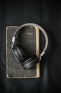 以黑皮革背景覆盖耳机的旧书剪贴版教学音乐桌子文学技术教育立体声教科书知识学习图片