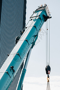 玻璃现代建筑附近带吊钩的蓝色起重机升降机构 起重机和液压升降机高达 120 米生长职场车辆工地汽车电梯折叠机器技术活动图片