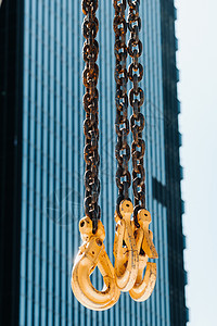 高楼玻璃附近的移动起重机的钩子 吊在吊起架上的链上挂有大量钩子绳索滑轮工具帮助天空商业机械仓库技术重量图片