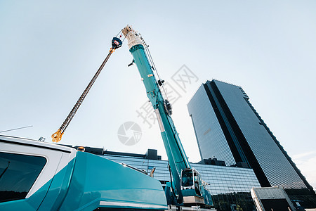 玻璃现代建筑附近带吊钩的蓝色起重机升降机构 起重机和液压升降机高达 120 米活动电梯折叠力量车辆机械技术生长天空科技背景图片