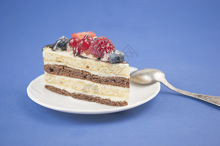 盘子上混合白莓切片蛋糕和蓝纸背景的旧汤匙美食食物奶油桌子蛋糕馅饼覆盆子面包糕点蓝色图片