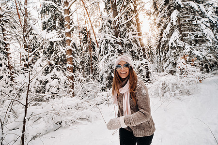 一个穿着毛衣和眼镜的女孩 在冬天在雪覆盖的森林里散步微笑树林女士头发成人新年女性快乐手套季节图片