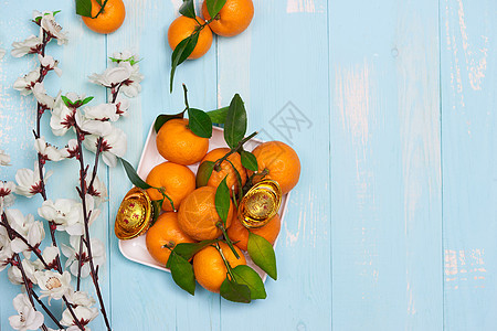 平铺中国新年的橘子橙子和木桌顶上的梅花家庭食物小吃西瓜糖果椰子月球种子红包红色图片