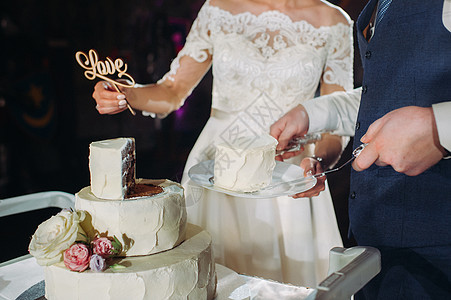 新娘和新郎切了他们的结婚蛋糕 漂亮的蛋糕 有一个切口和可见的馅料 与词爱的婚宴喜饼 婚礼的概念装饰品巧克力食物桌子夫妻木头戒指仪图片