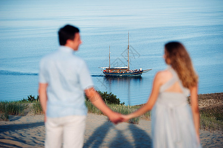 一对相爱的情侣站在沙丘的海滩上 背景是波罗的海和一艘船 一对情侣在立陶宛尼达的海滩特写奢华地平线蓝色夫妻恋人天空海岸线运动旅行帆图片