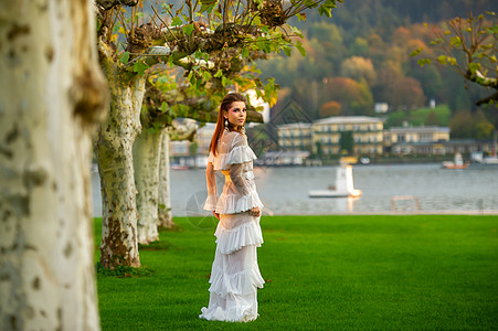 穿着白婚礼服的新娘 位于奥地利城镇的一个公园中 日落时有大树长裙婚纱空气村庄建筑学树木女士压痛裙子青年图片