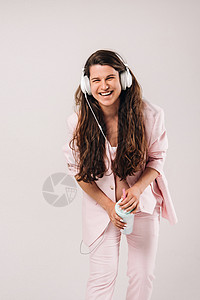 一个穿粉红色西装 带耳机的孕妇 在情感上聆听灰色背景的音乐图片