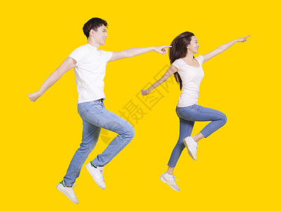 年轻夫妇在复制空间上跳跃和指手画脚 在黄色背景上孤立无援图片