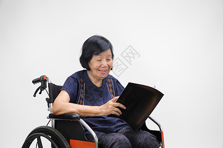 年长的亚裔女性在阅读白色背景杂志时微笑图片